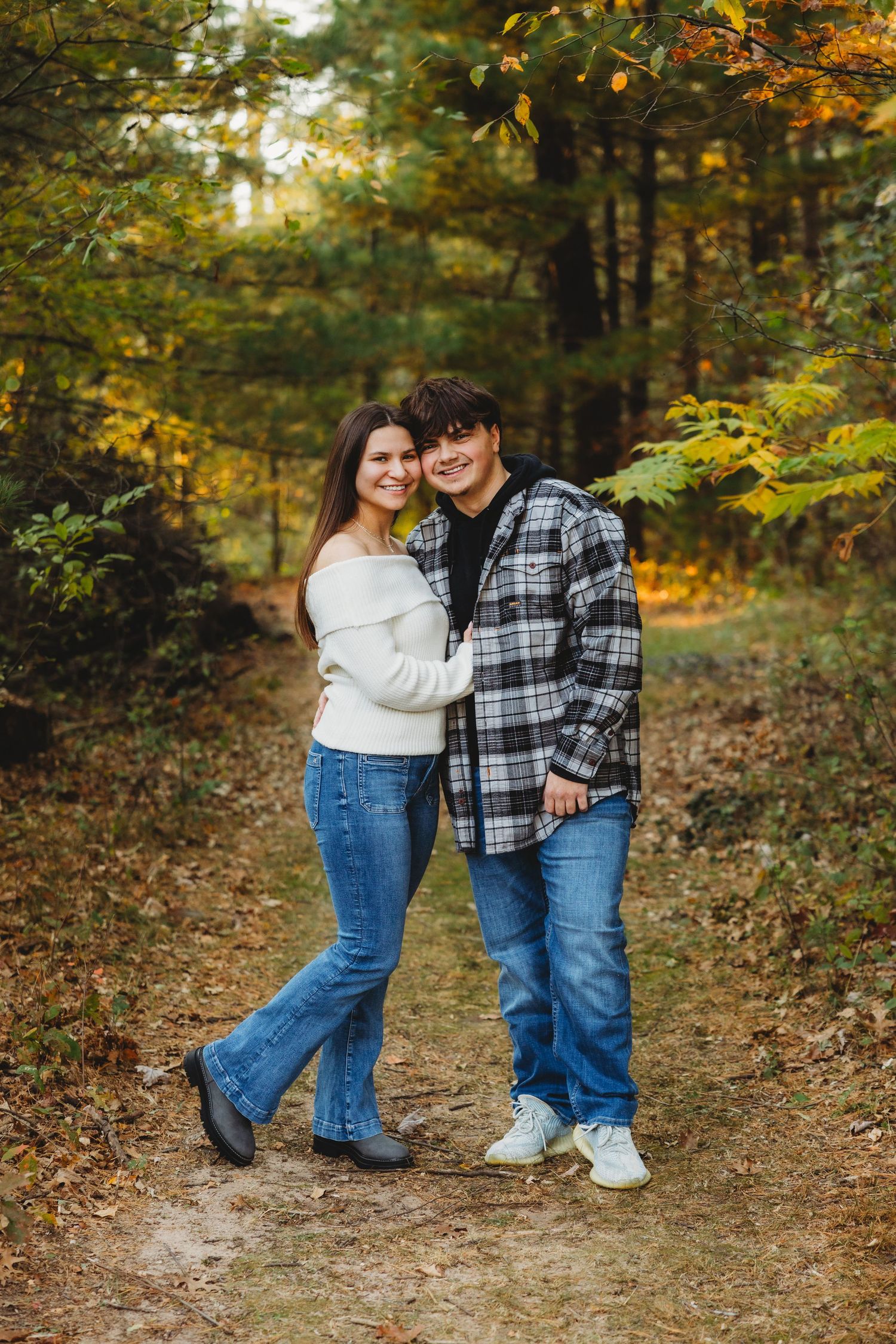 A couple embraces on an autumn forest path surrounded by golden foliage and fallen leaves.