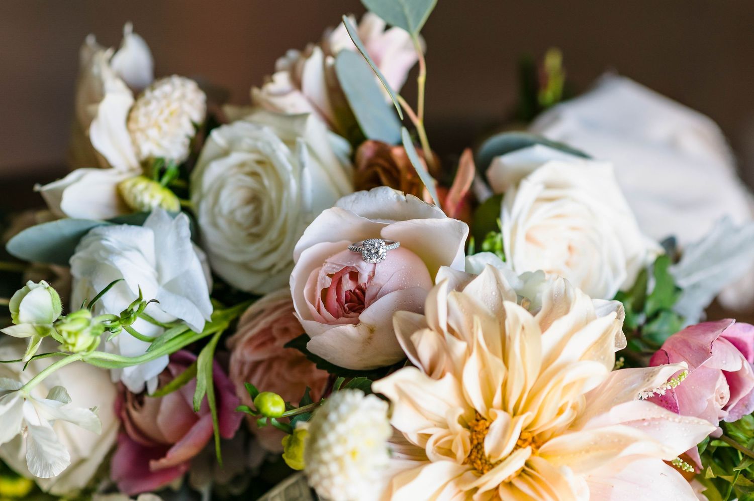 An elegant diamond engagement ring nestled in a navy blue velvet box surrounded by delicate floral arrangements.