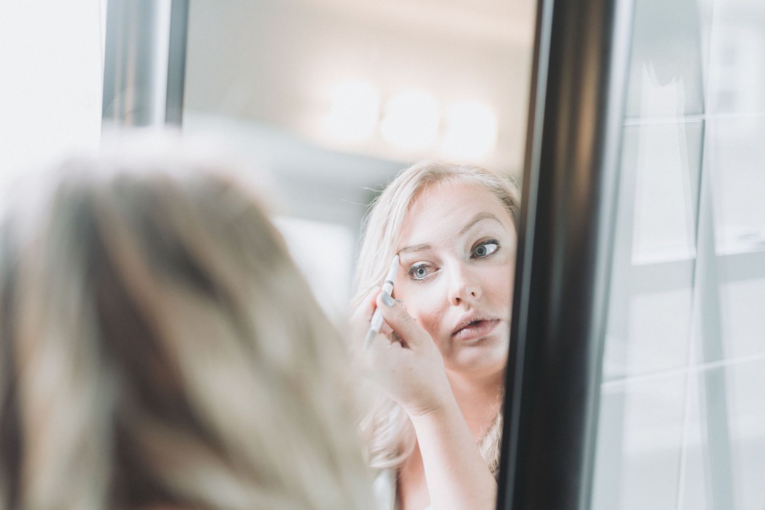 A woman with blonde hair and smokey eye makeup gazes at her reflection in a mirror.