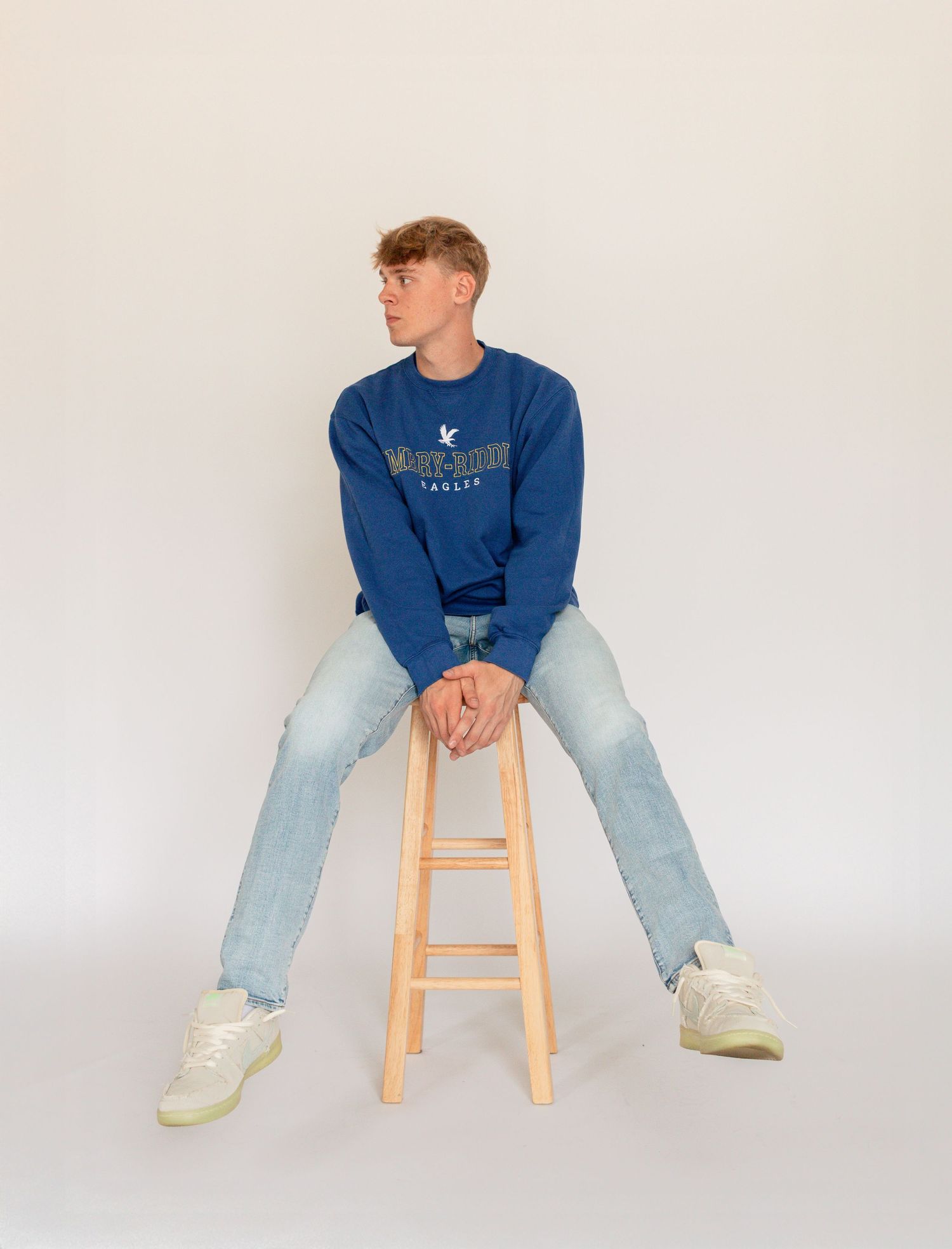 Person in blue sweatshirt and light jeans sits casually on wooden stool against white backdrop in four similar poses.Family, senior, and wed