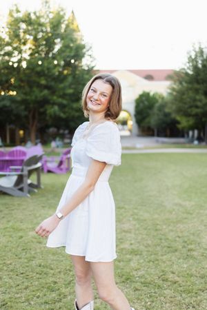 A person in a white summer dress twirls playfully in a grassy outdoor setting during golden hour.