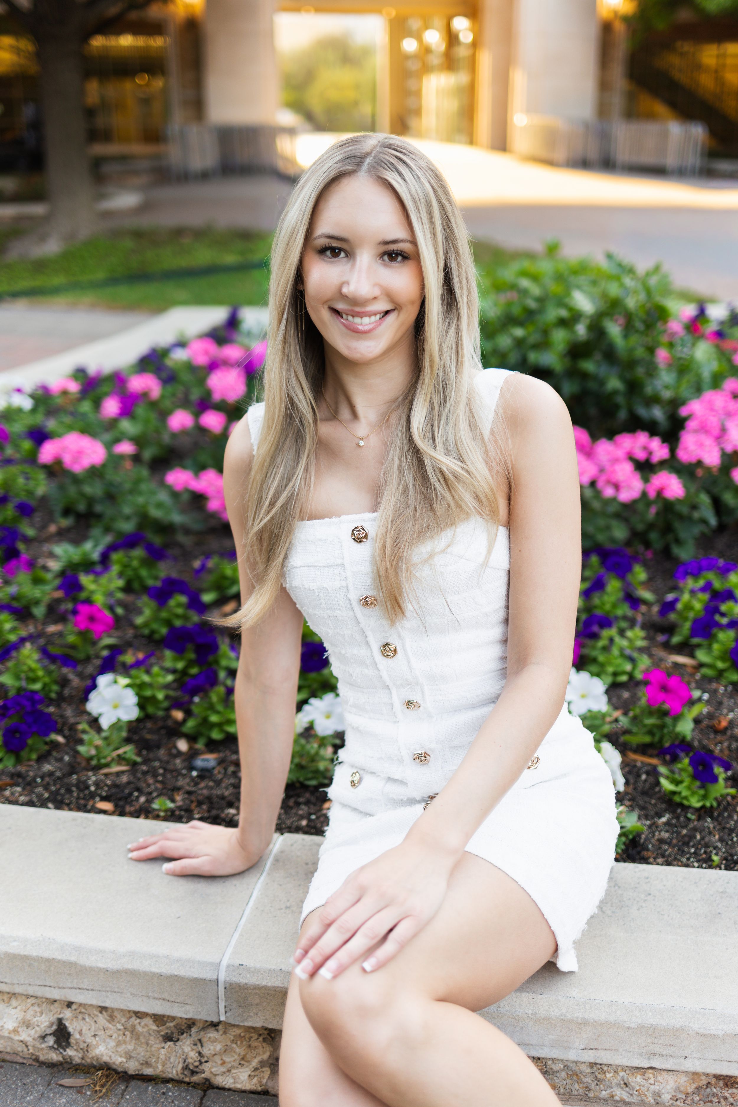 A series of outdoor portrait photos featuring someone in a white button-up sundress sitting near pink and purple flowers.