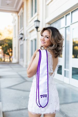 Woman in white sleeveless top with purple TCU trim poses outdoors against building exterior in lifestyle photoshoot.