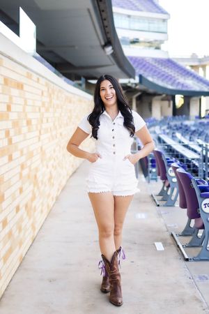 A person in a white dress and brown boots poses in an empty stadium concourse area.