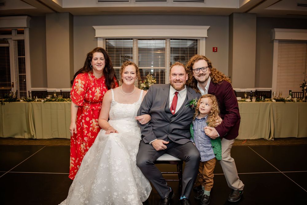 Wedding party poses together in a banquet hall with red and black formal attire.