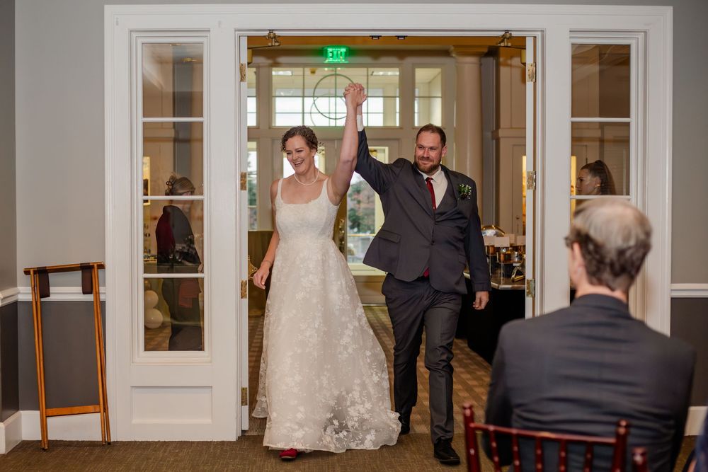 A bride and groom make their grand entrance into a wedding reception hall as guests applaud.