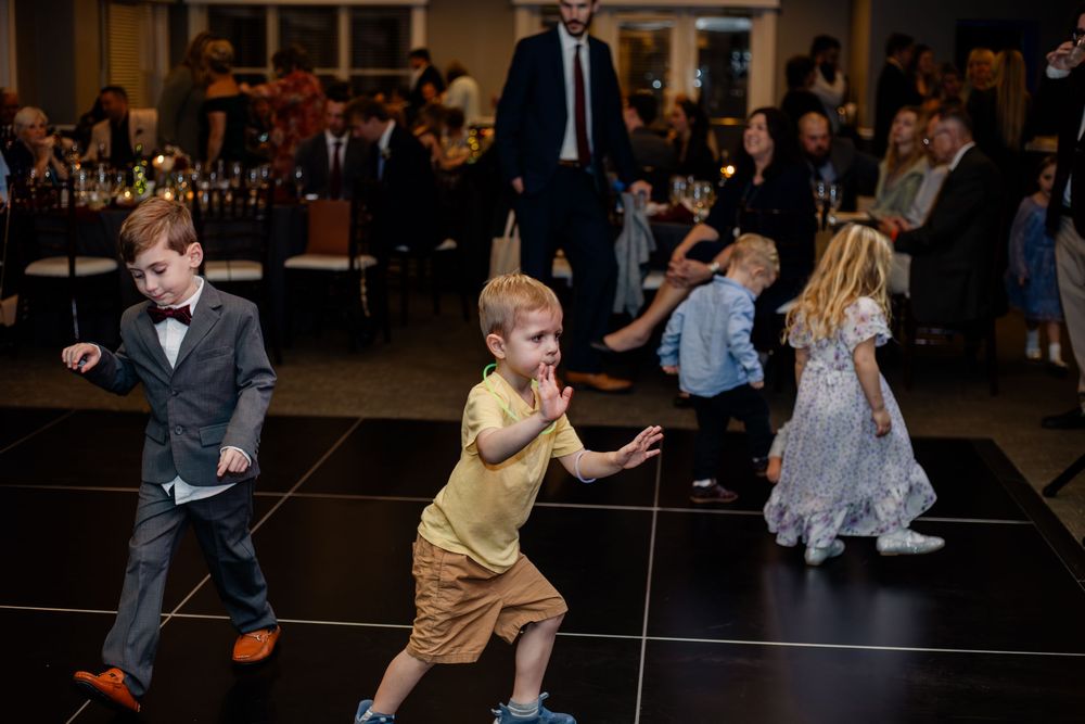 A group of people dancing energetically at what appears to be a wedding reception or party on a dark dance floor.