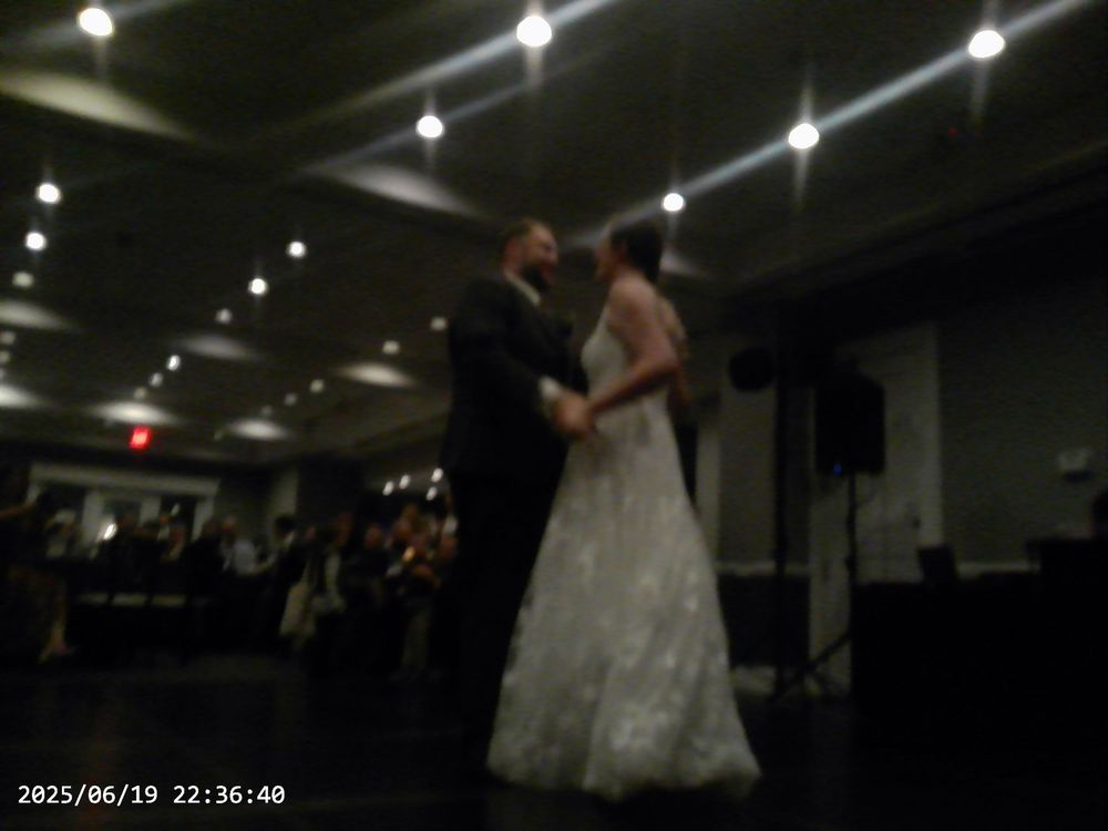 A couple in formal wedding attire dances together during their first dance at an indoor reception venue.