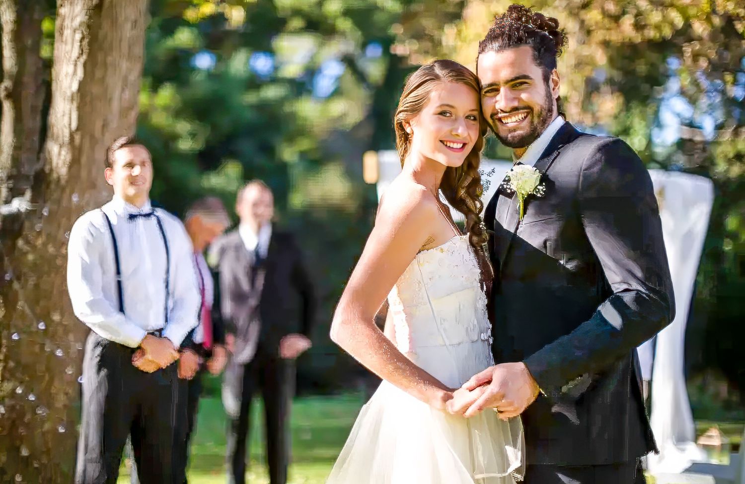 Wedding couple embraces and laughs together during outdoor photo session in lush green garden setting.