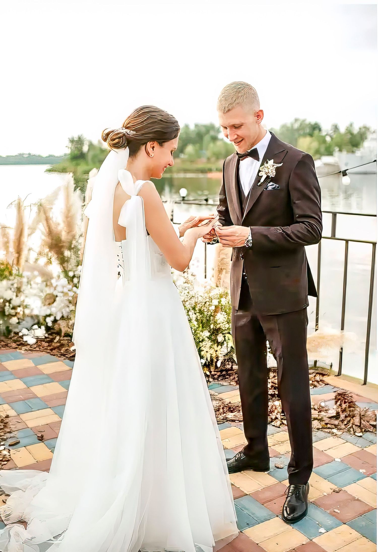 Romantic wedding couple shares intimate moments on an outdoor patio with decorative pampas grass and waterfront views.