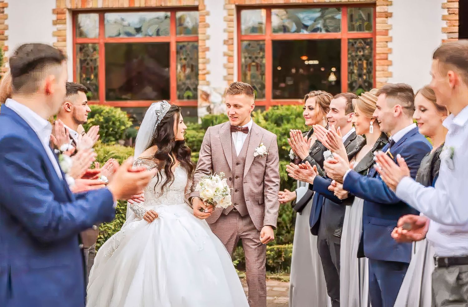 Wedding party guests celebrate and toast with champagne glasses at an outdoor reception by a brick building.