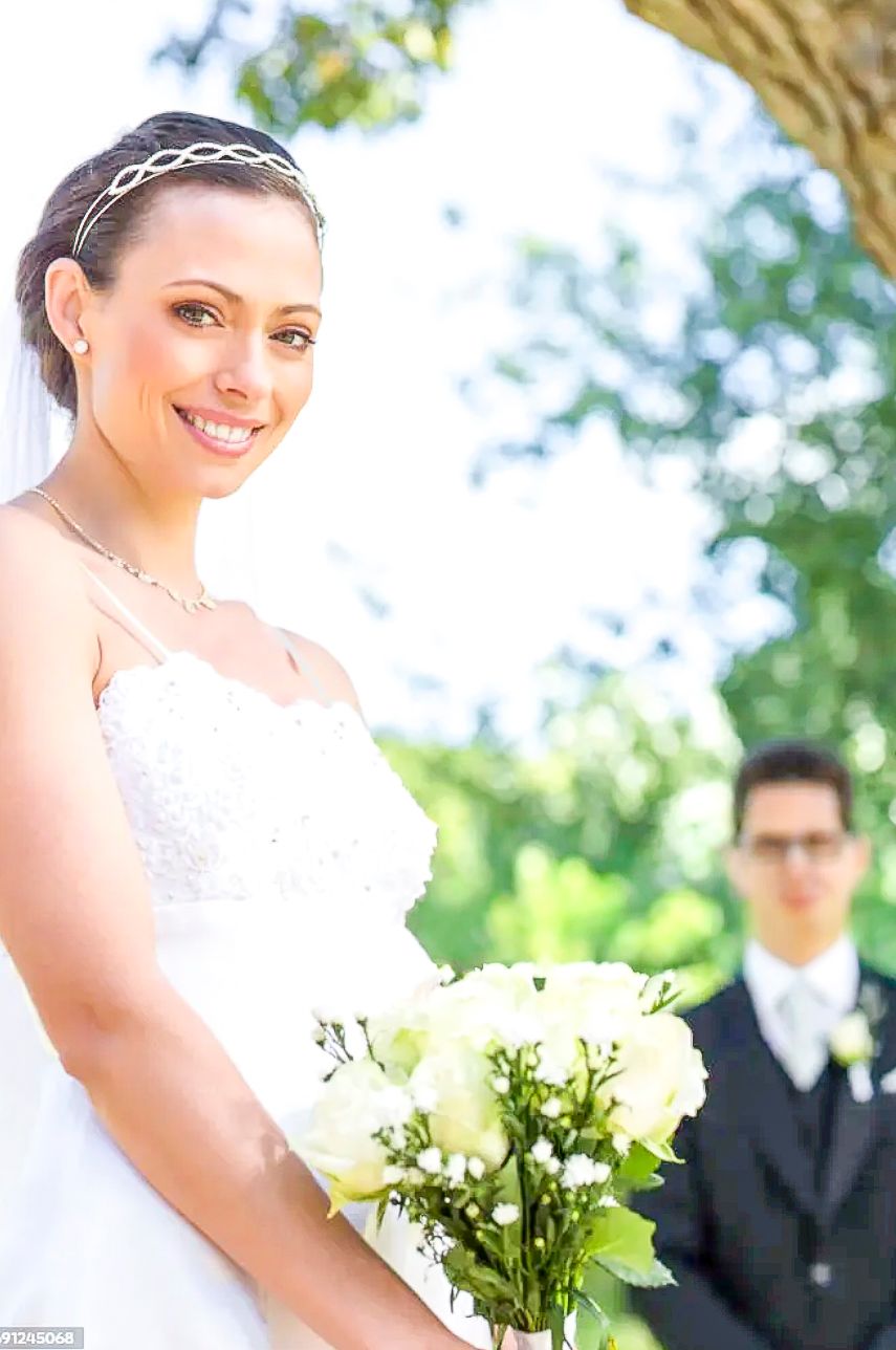 A bride in a white wedding dress holds a bouquet of white flowers in an outdoor garden setting.
