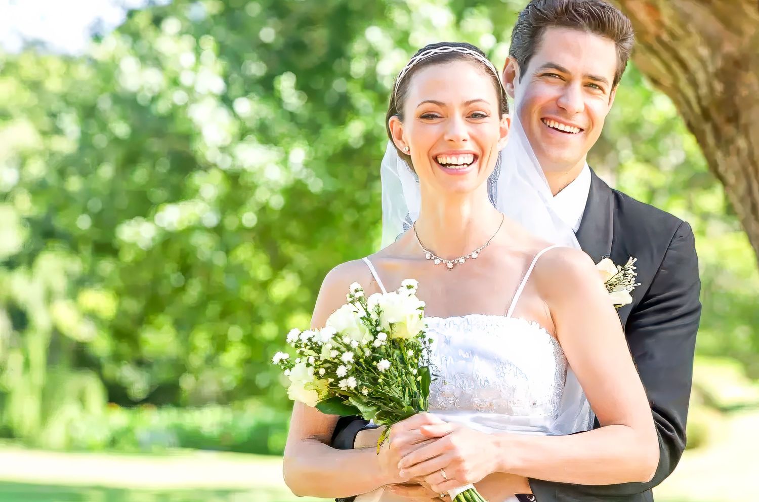 A happy couple shares a joyful moment together outdoors on their wedding day surrounded by lush greenery.