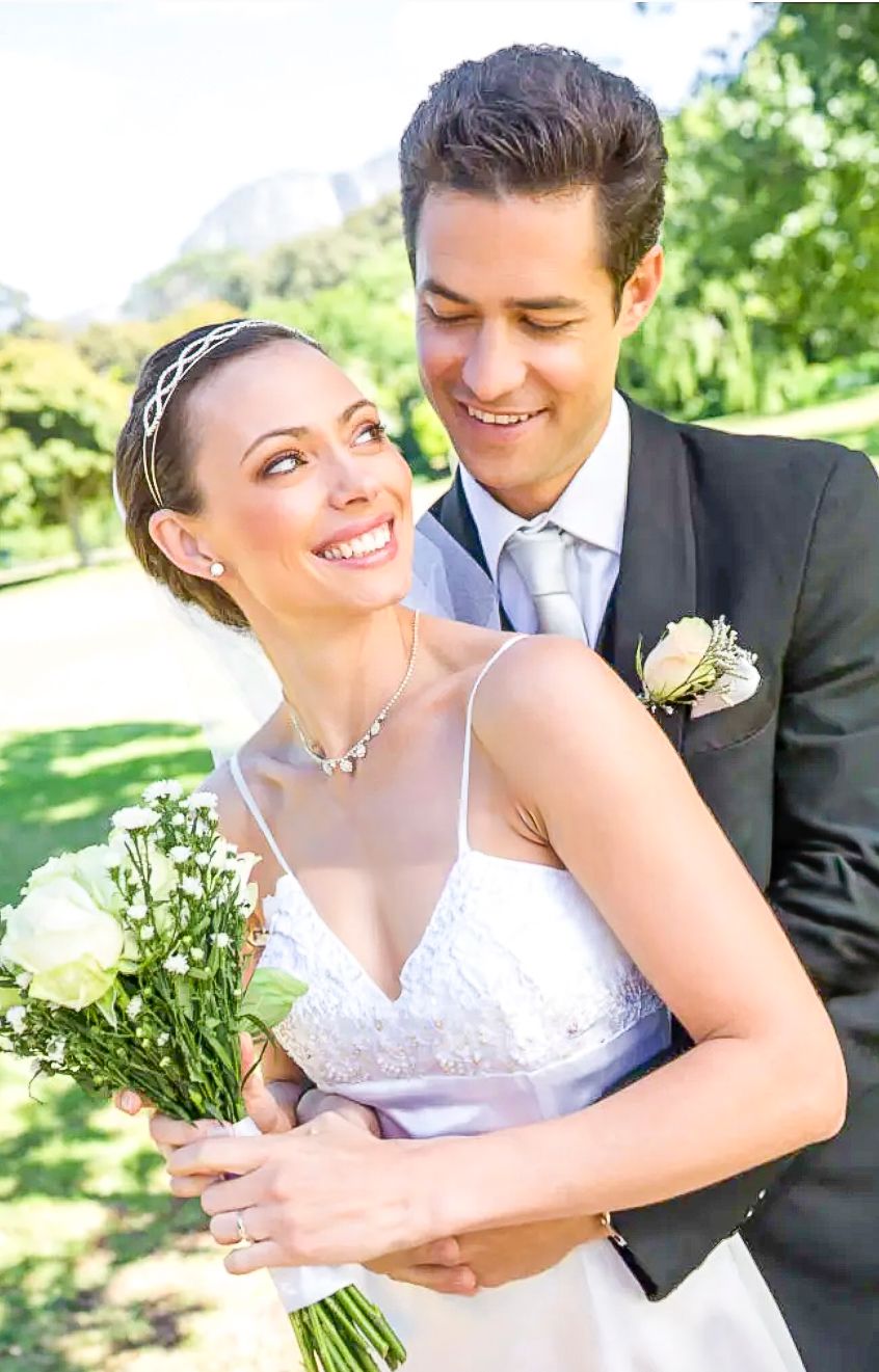 Happy newlyweds share a tender moment outdoors holding a bouquet of white flowers on their wedding day.