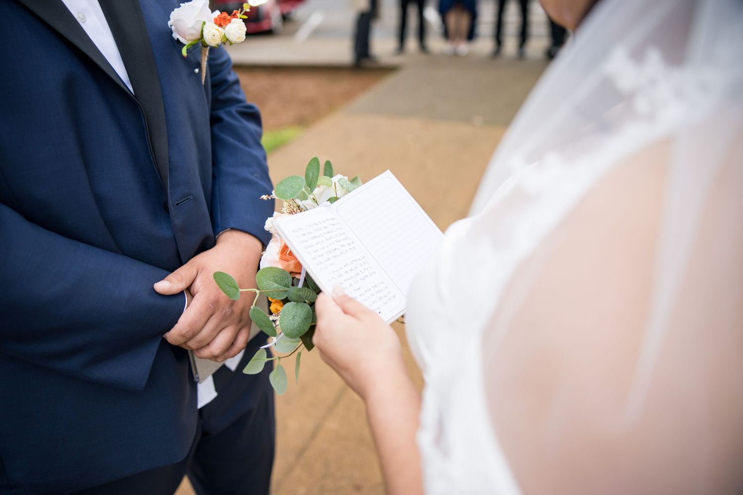 Close up of a white rose boutonniere being pinned on a navy blue suit jacket at a formal event.