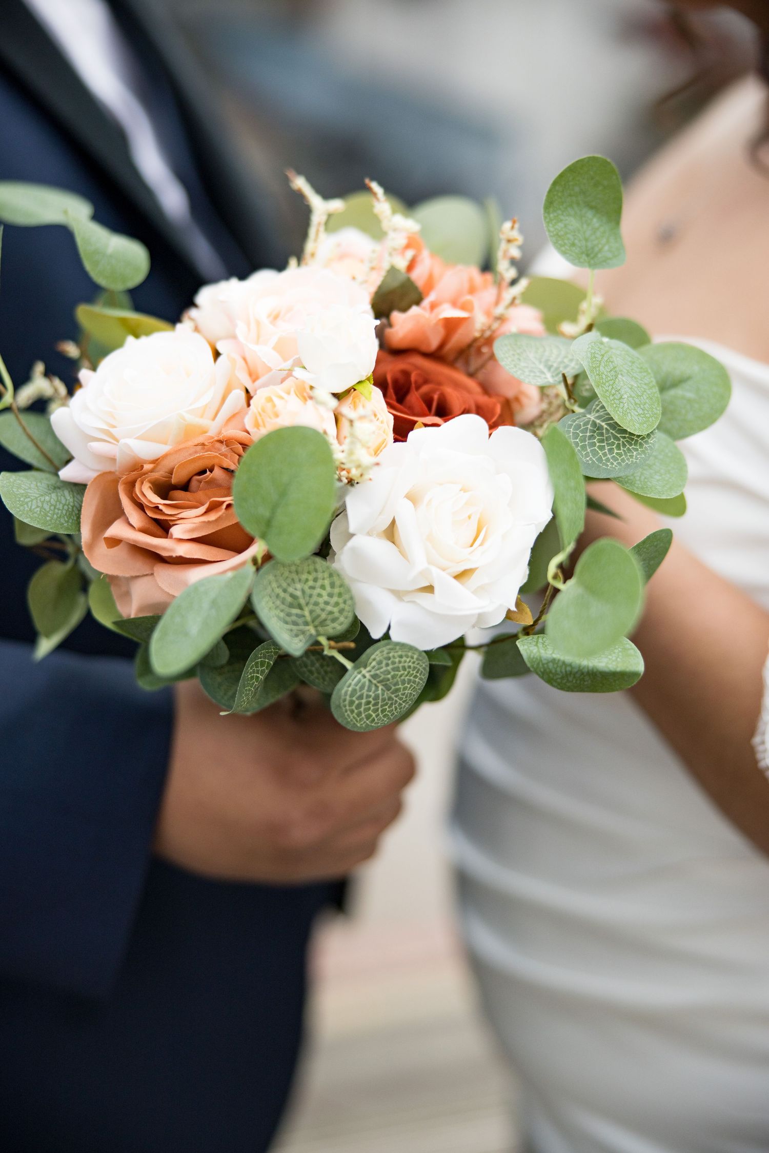 A close-up of a wedding bouquet featuring peach and white roses with eucalyptus greenery.