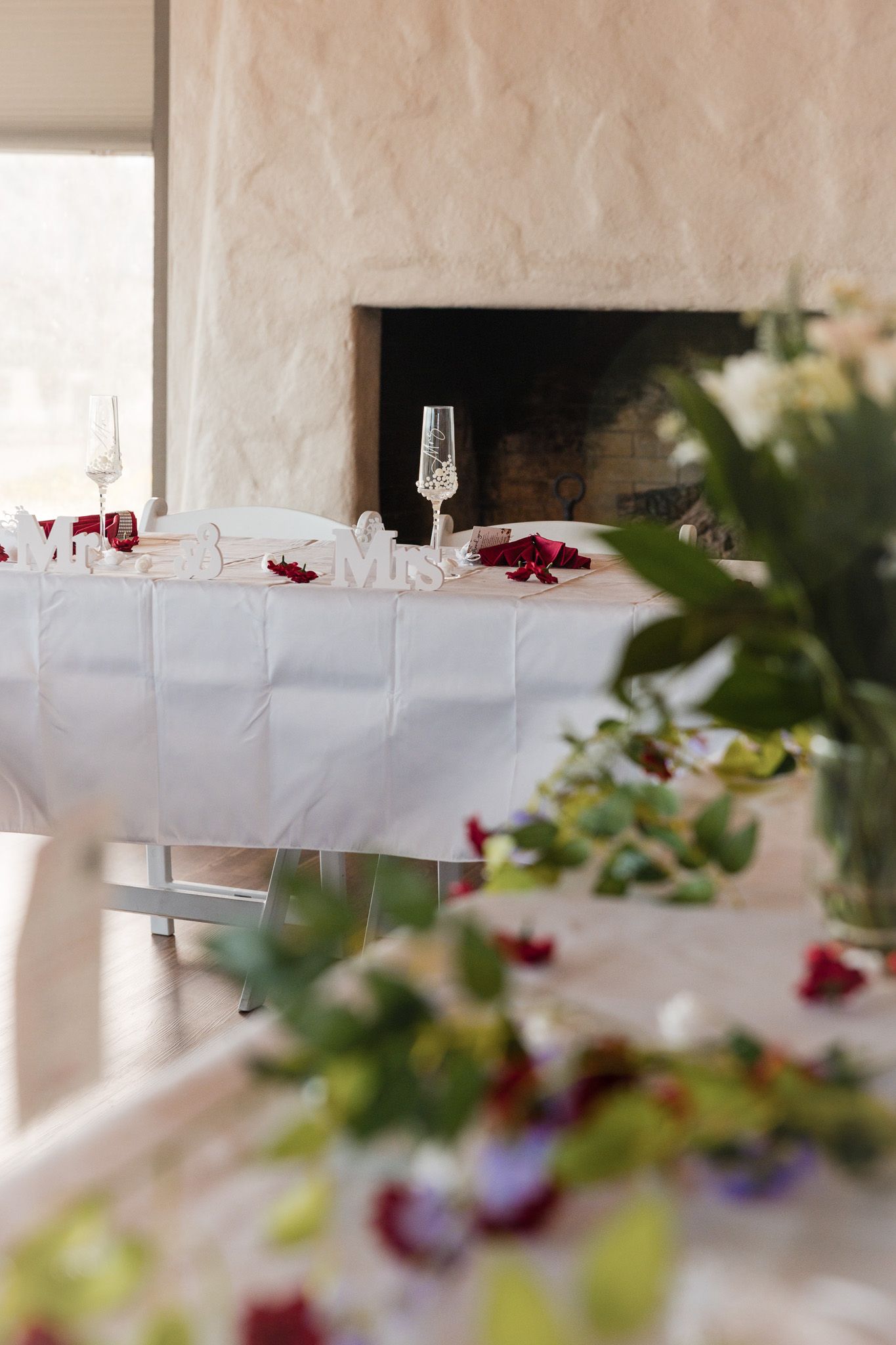 Elegant white tablecloth dining tables decorated with red floral accents and crystal glassware for a formal event.