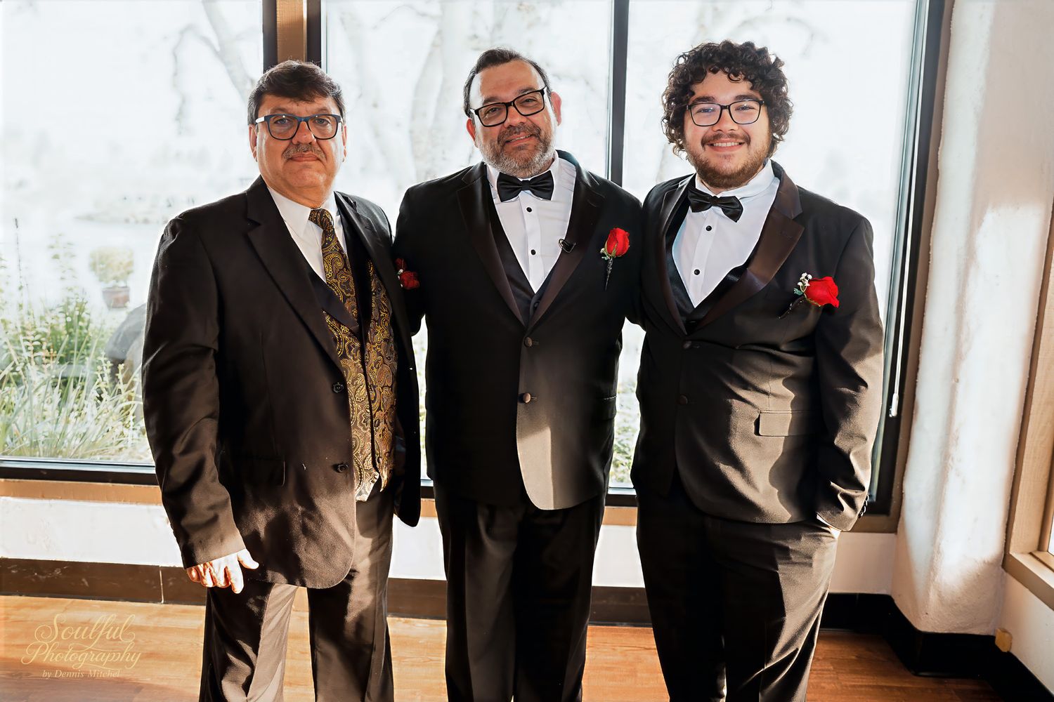 A group of men wearing black tuxedos and bowties stand together in a formal setting.