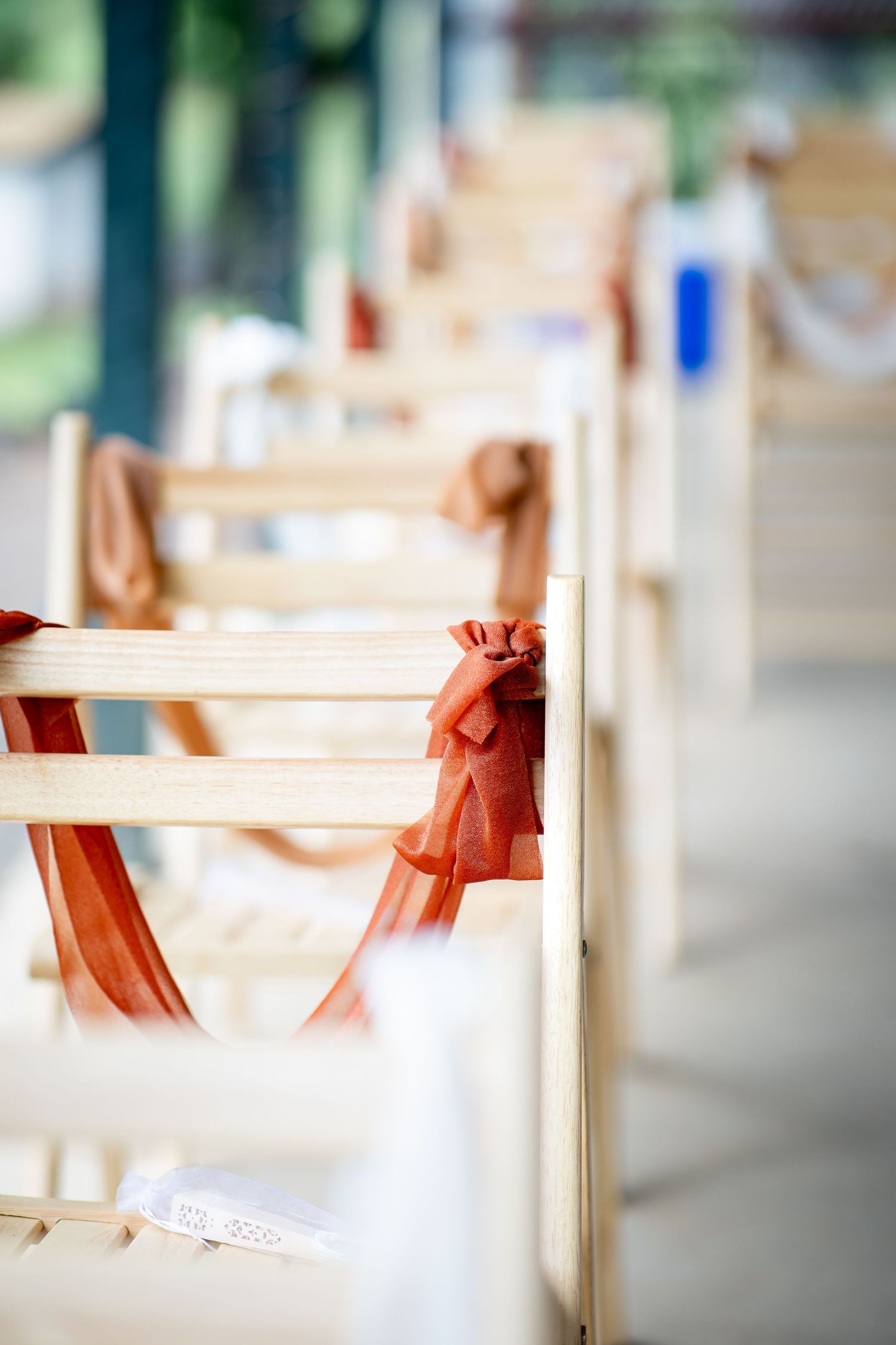Wooden wedding ceremony chairs decorated with elegant rust-orange ribbon bows arranged in rows for an outdoor celebration.