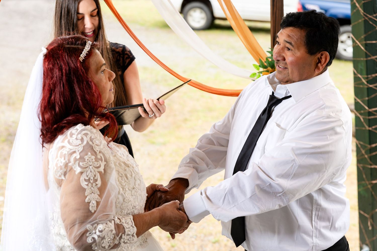 Bride and groom holding hands during outdoor wedding ceremony under decorative orange arch.