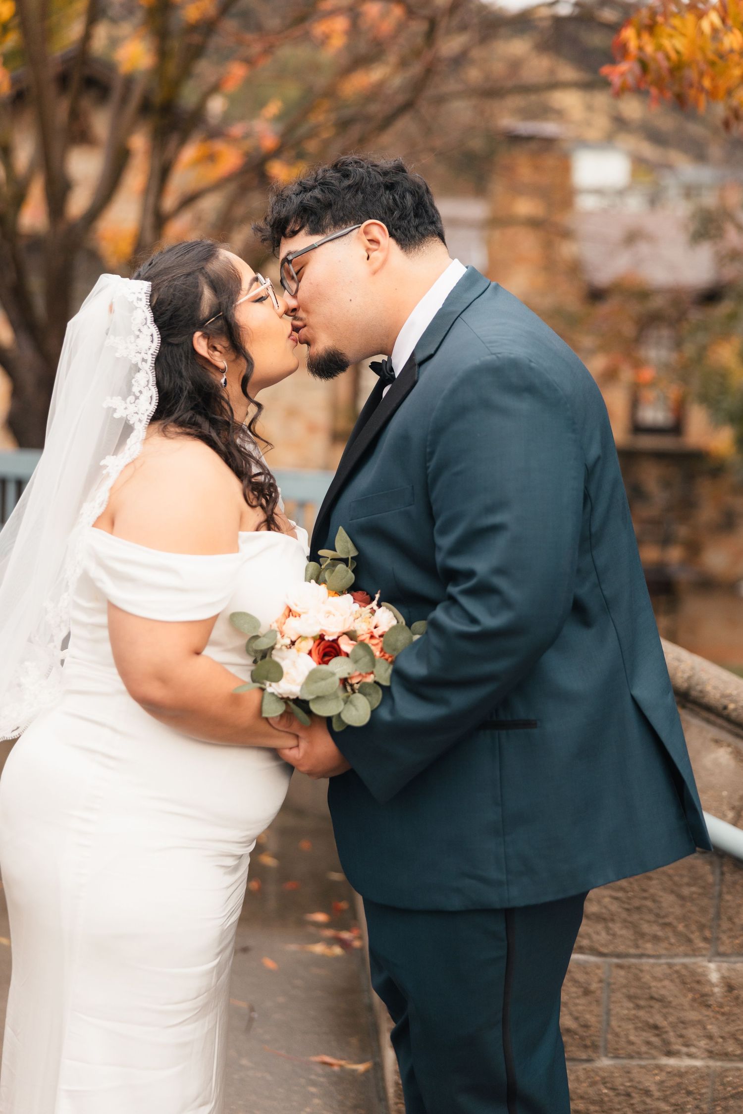 A romantic wedding moment captured in autumn with fall foliage in the background.