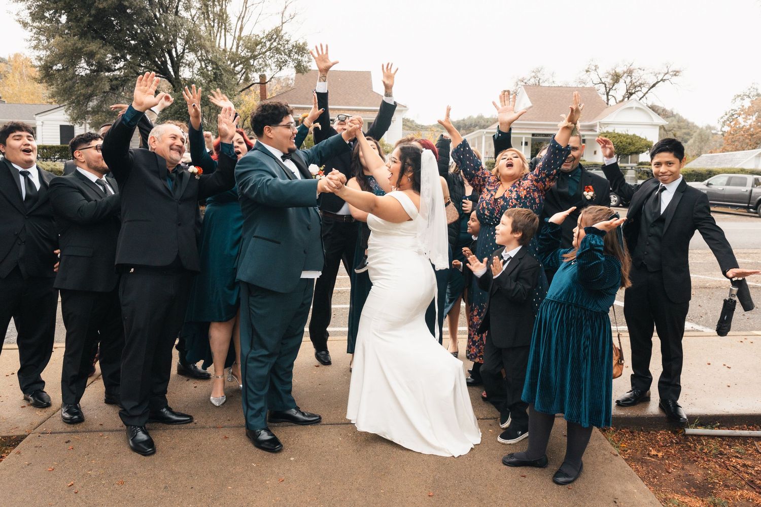 Wedding party in formal attire jumps together outside in a synchronized celebratory pose.