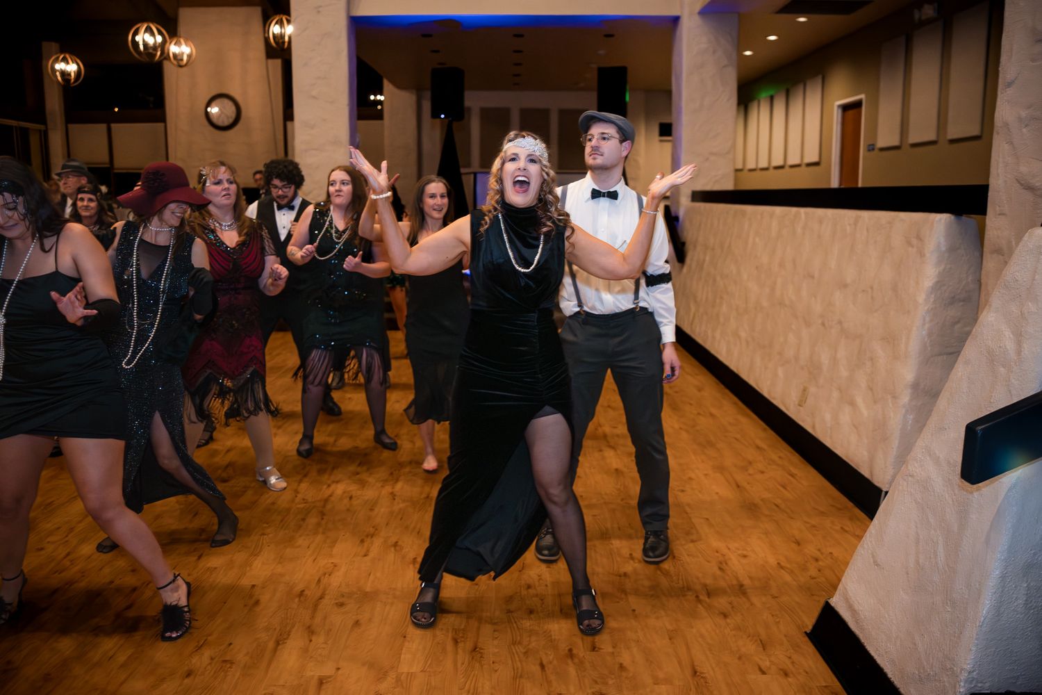 People dancing together in a wooden-floored ballroom with warm lighting and rustic decor.