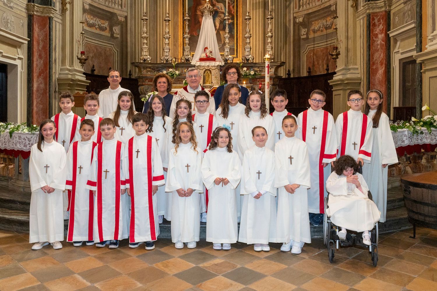 Group portrait of young confirmands in white robes with red stoles standing in church.