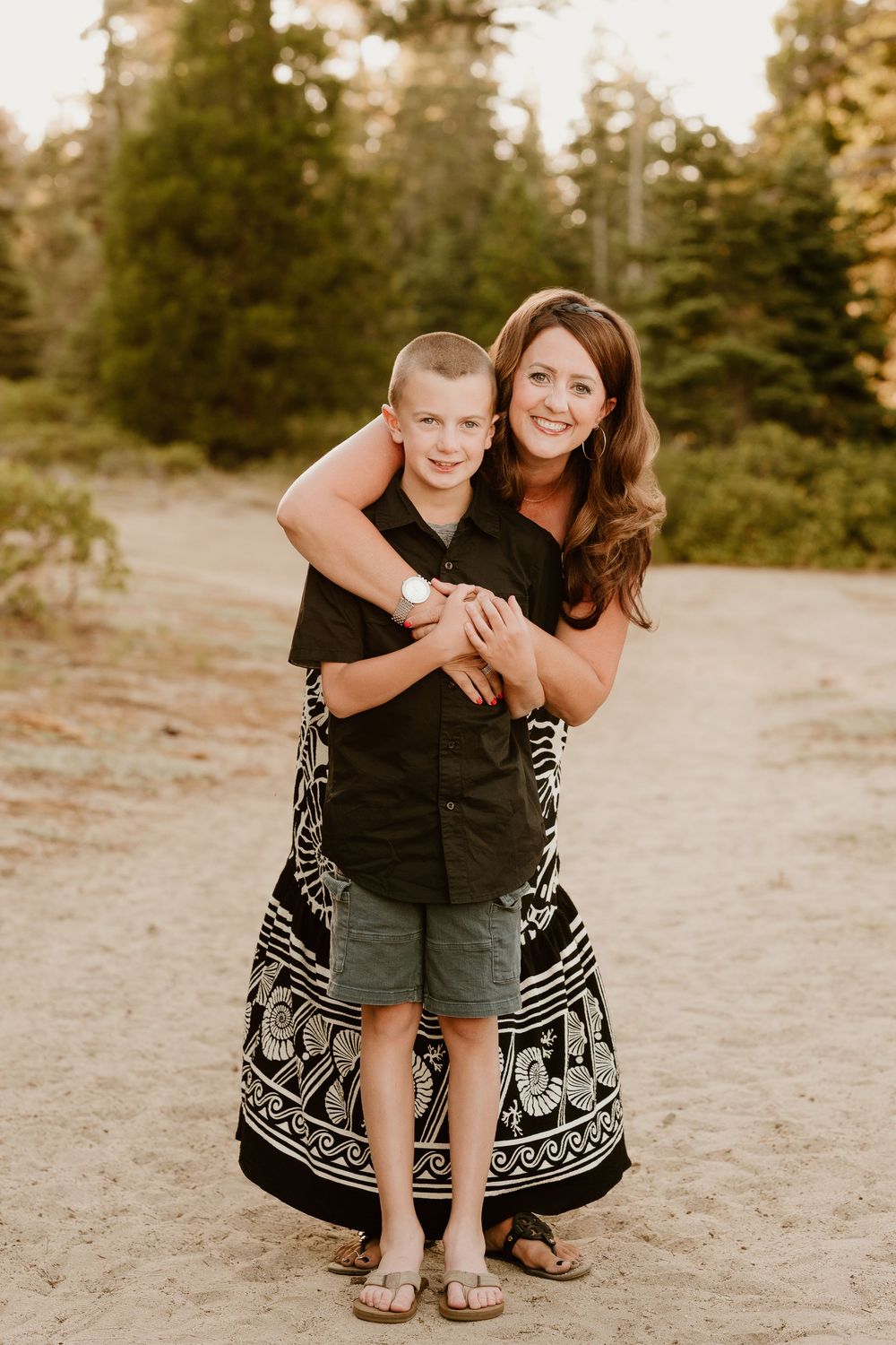 A parent and child share a tender moment outdoors in matching black outfits against a natural background.