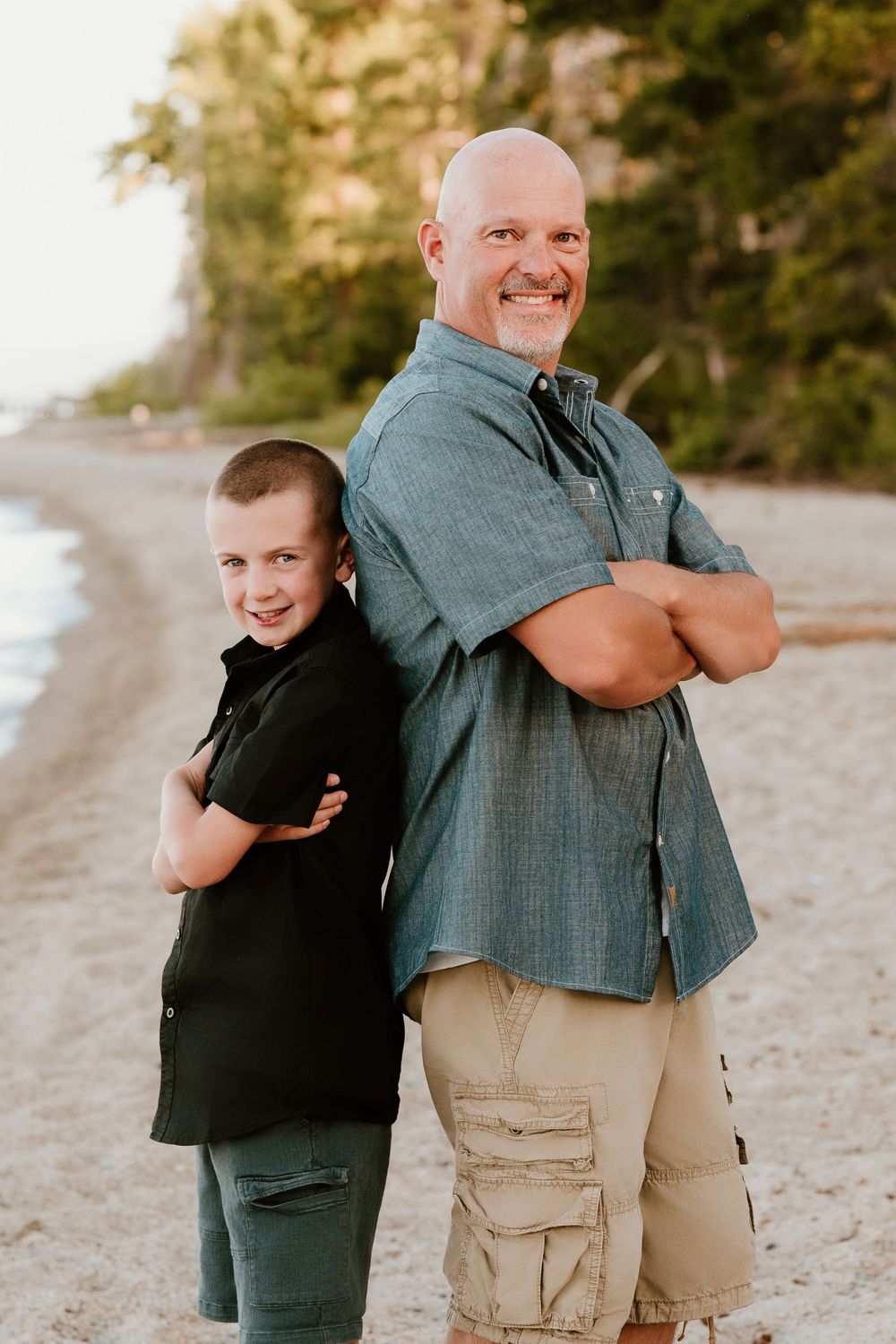 Two people stand back-to-back with crossed arms on a beach path during golden hour.