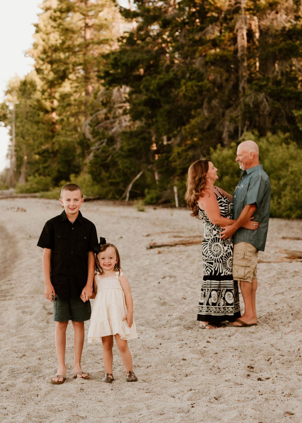 Family portrait at sunset on a sandy beach with pine trees in the background during golden hour.