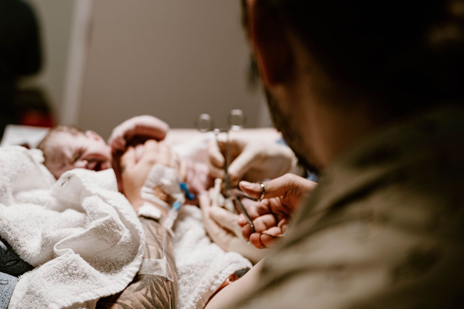 A newborn baby yawns while wearing a striped hospital cap and white swaddle blanket.