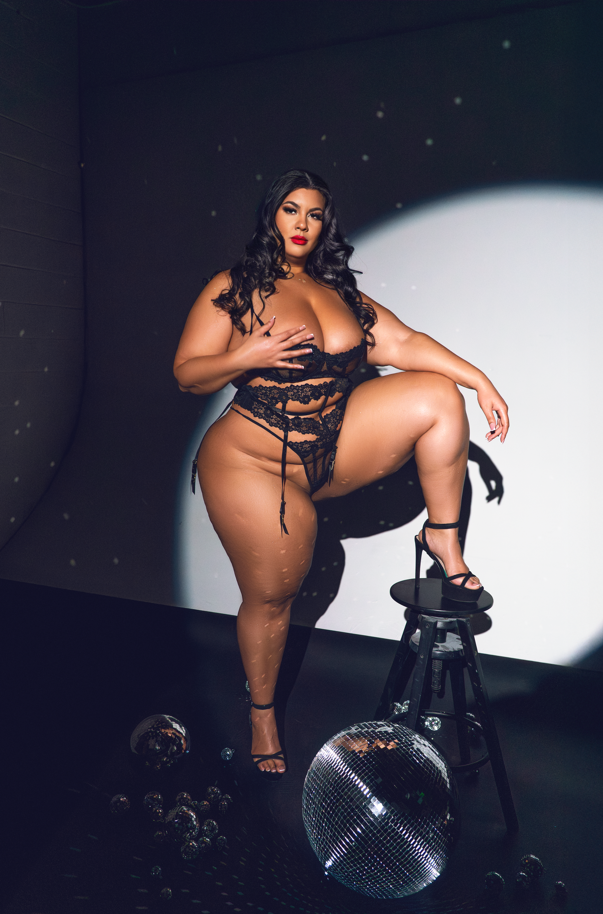 Artistic boudoir photoshoot with black lace lingerie and disco ball in dark moody lighting.