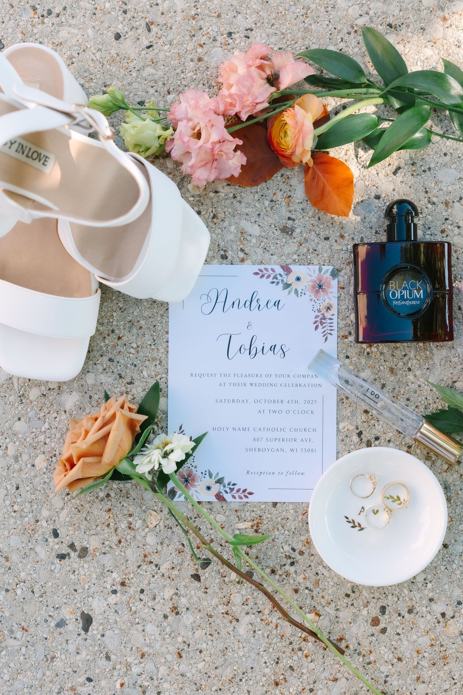 A pair of elegant white bridal shoes with pointed toes and delicate details displayed on a rustic wooden surface.