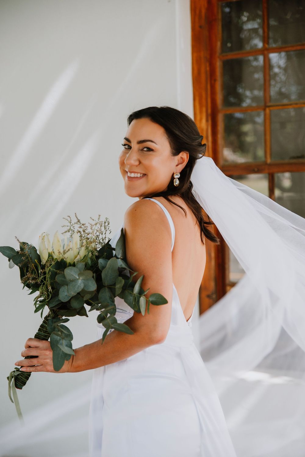Bride smiling over her shoulder holding her bouquet, with her veil softly framing the image in an elegant bridal portrait