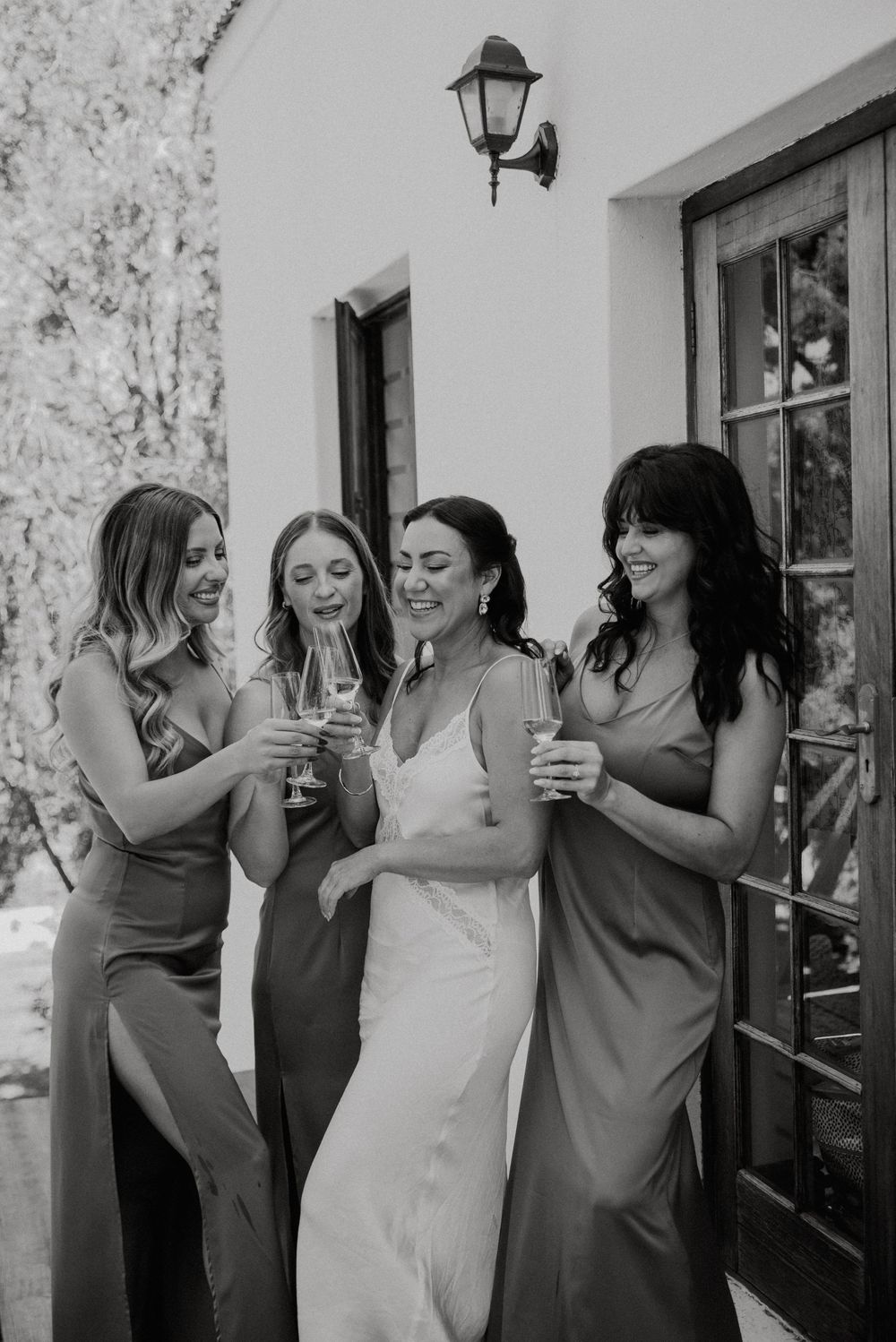 Black and white photo of bride and bridesmaids sharing a celebratory toast, capturing a joyful wedding moment