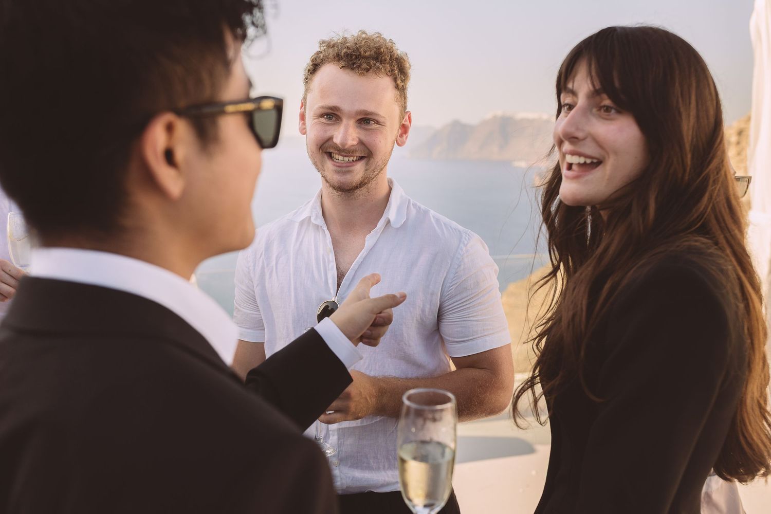 Group of Santorini wedding guests enjoying drinks and conversation outdoors on a sunny afternoon at El Viento.