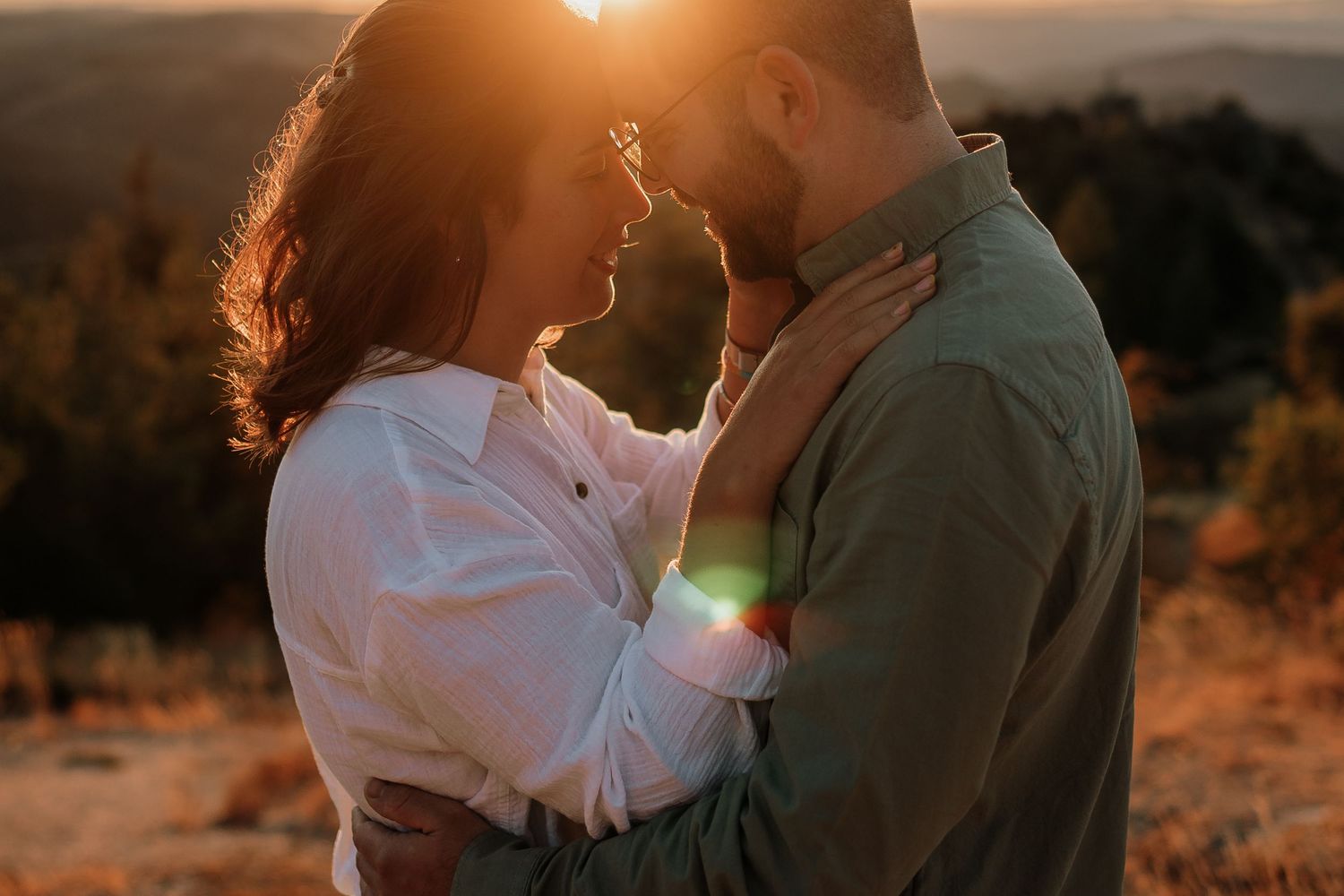 A couple embraces in front of a rustic red barn wall with white trim and windows during a romantic photoshoot.