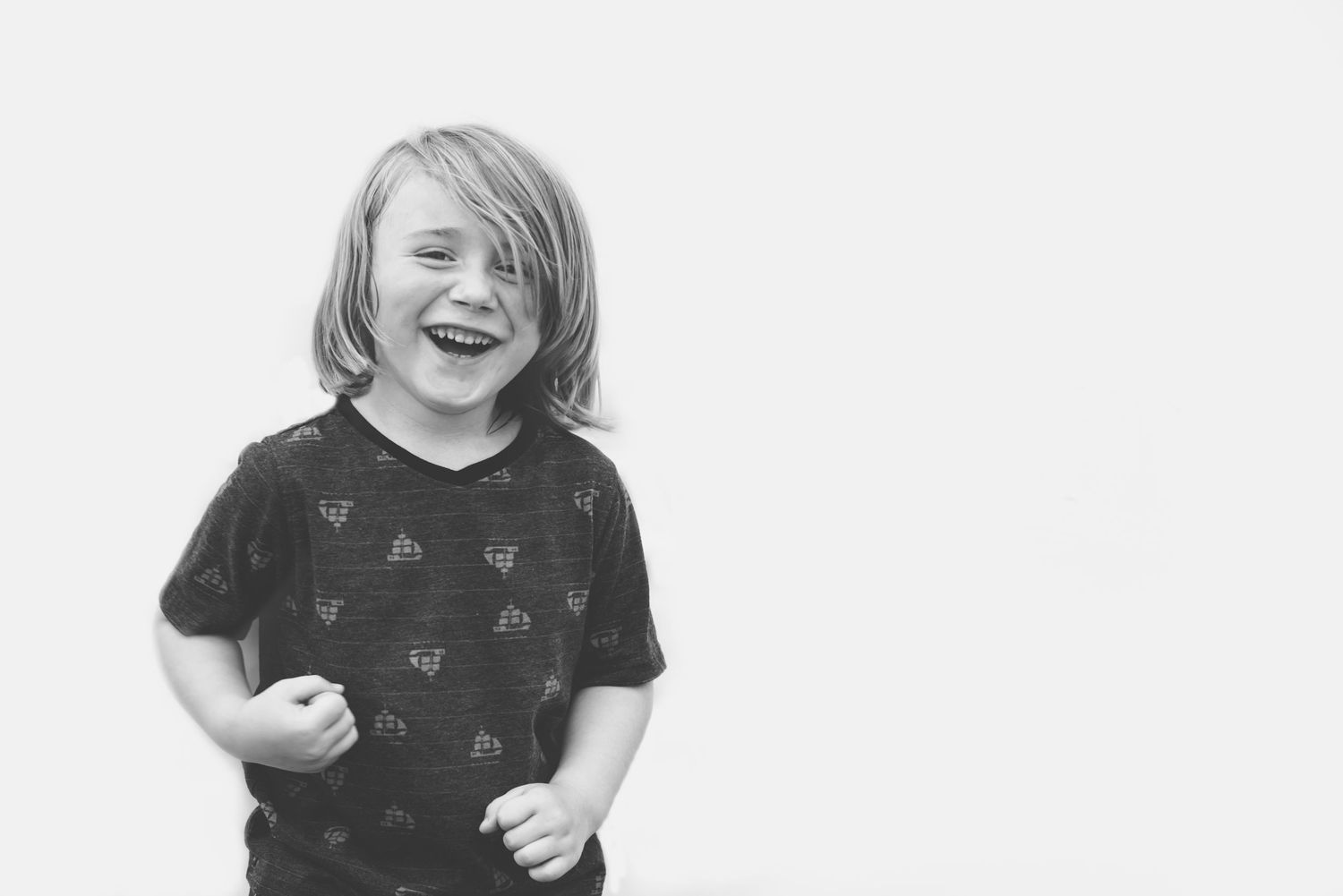 A black and white photo of a child laughing while wearing a dark t-shirt with a butterfly pattern.