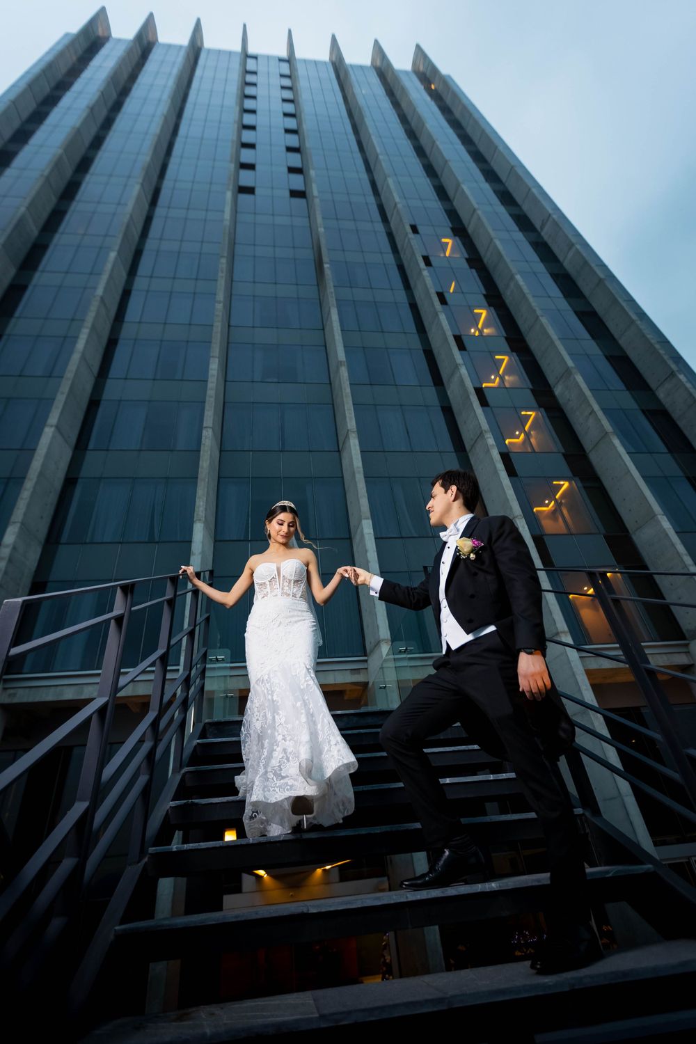 Dramatic wedding portrait on industrial stairs against modern glass building facade.