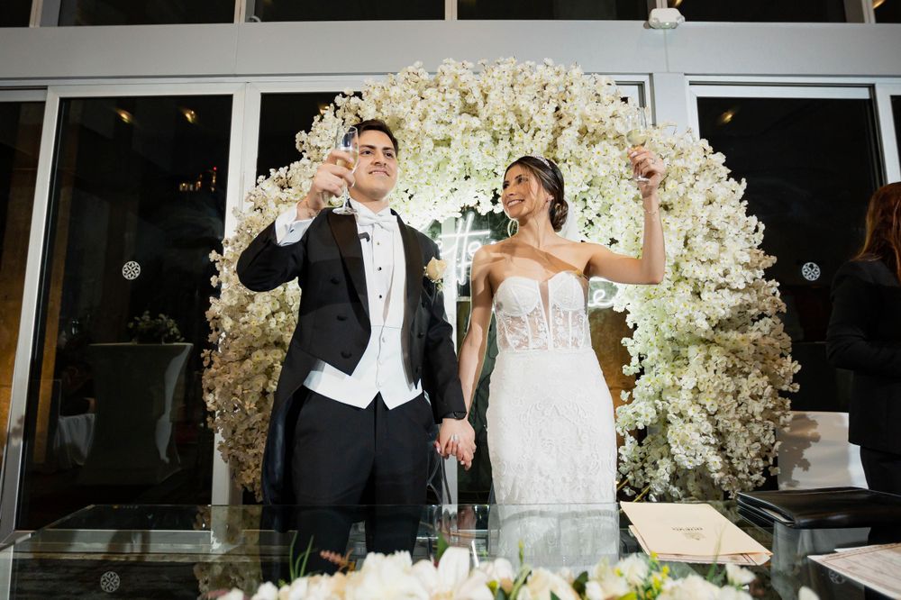 Wedding couple celebrates joyfully under a magnificent white floral arch during their reception.
