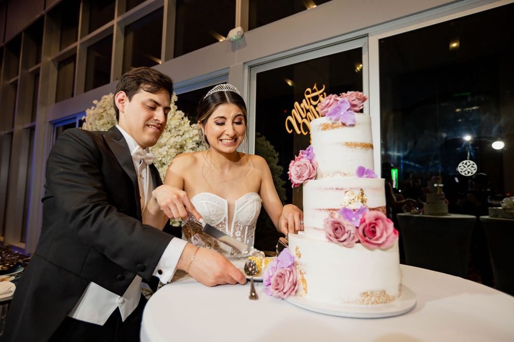 Couple cutting an elegant pink and gold wedding cake decorated with fresh flowers during their reception celebration.
