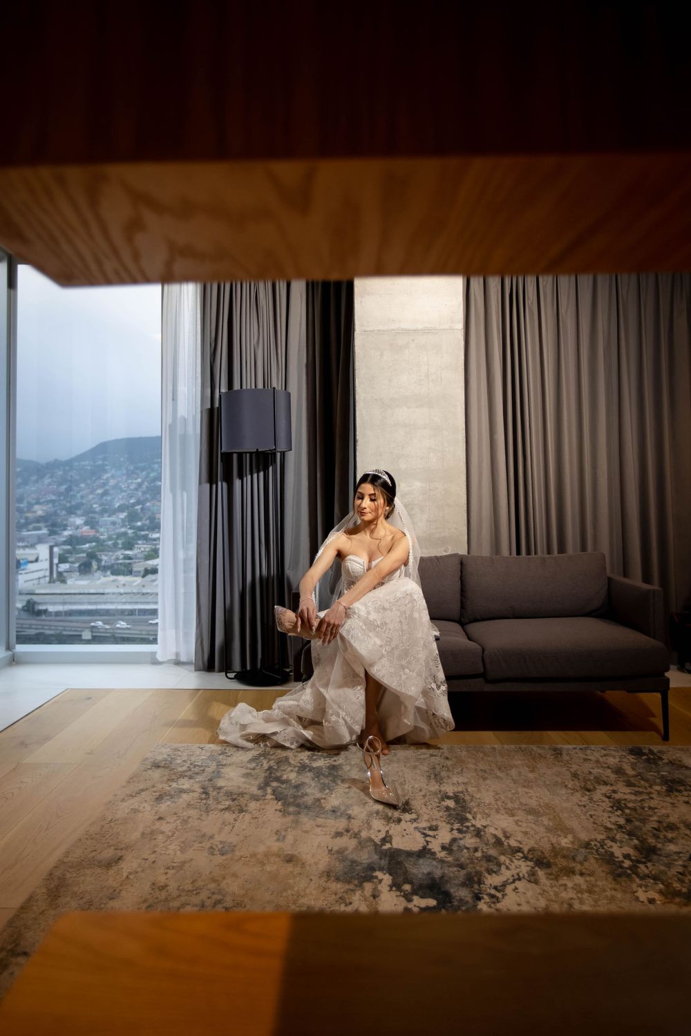 Elegant bride sits on couch in modern room with mountain views through large windows.