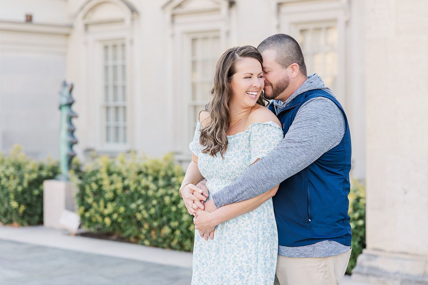 A loving couple embraces while sharing a tender moment outside an elegant white building.