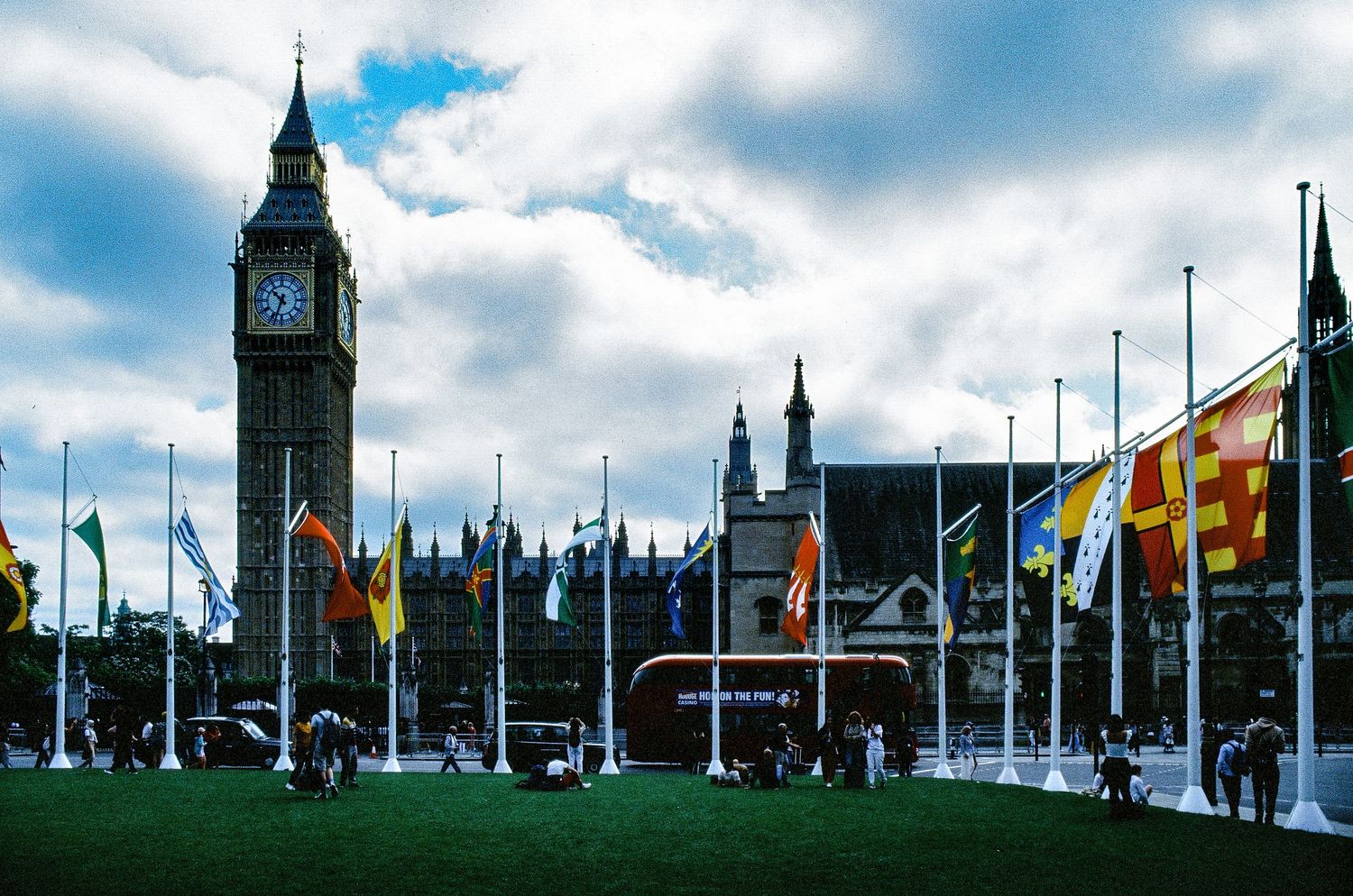 London's iconic Big Ben and Houses of Parliament with international flags flying in Parliament Square on a cloudy day.
