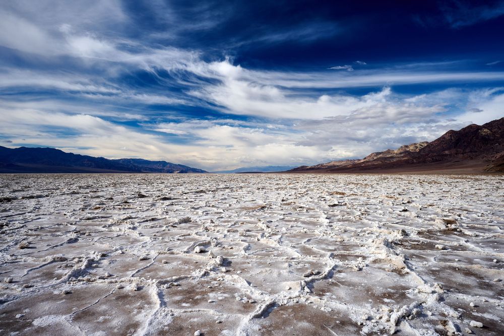 Salt flats stretching across Death Valley with dramatic clouds and mountains in the background.