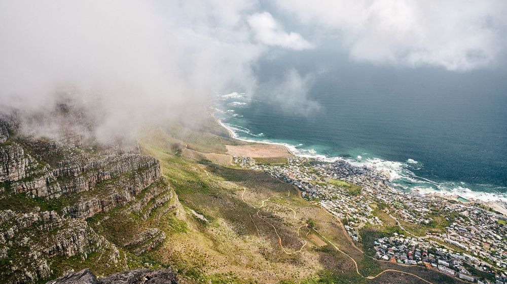 Aerial view of a coastal town nestled between mountains and ocean with dramatic fog rolling in.