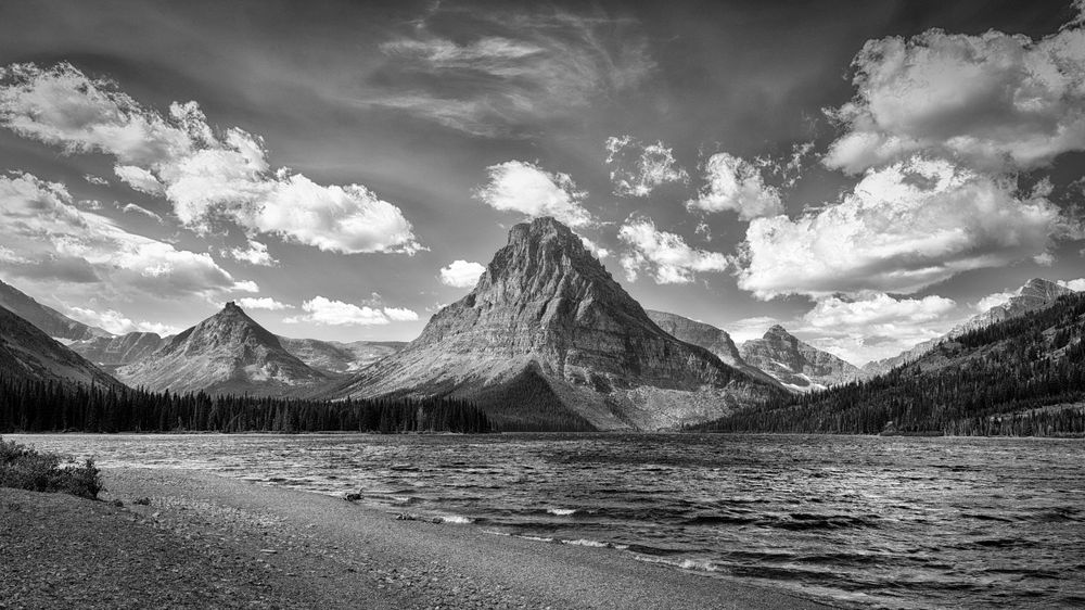 Sweeping panoramic view of majestic mountain peaks under dramatic cloudy skies in a wilderness landscape.