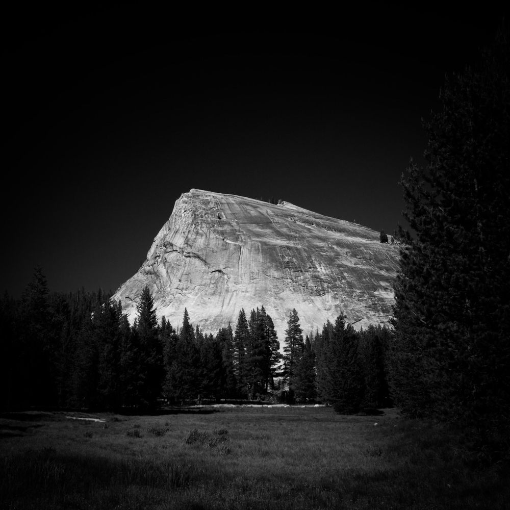 Black and white landscape of mountain peaks with evergreen trees in silhouette.