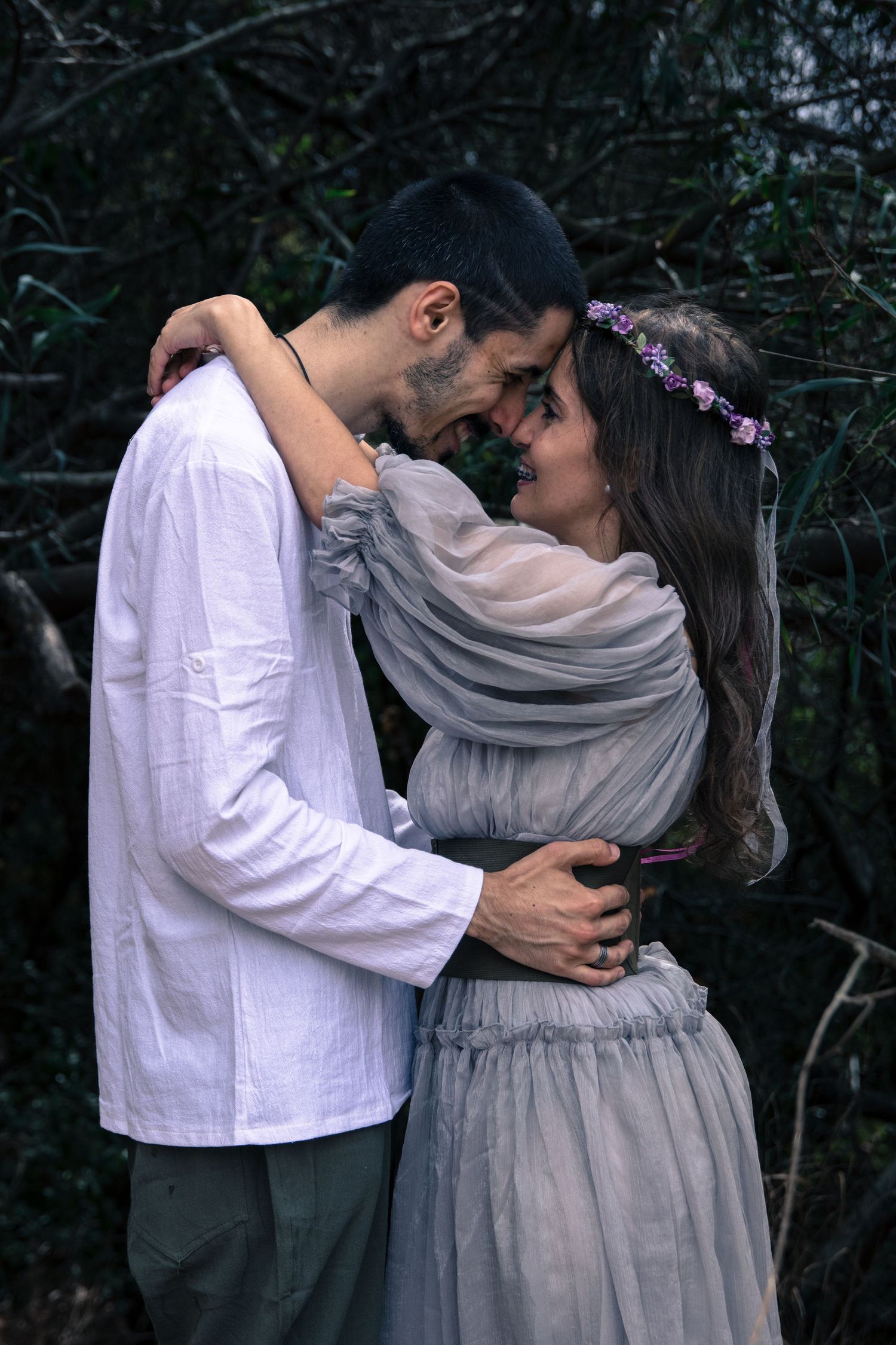 Intimate couple photoshoot in grey and white attire against dark forest background.